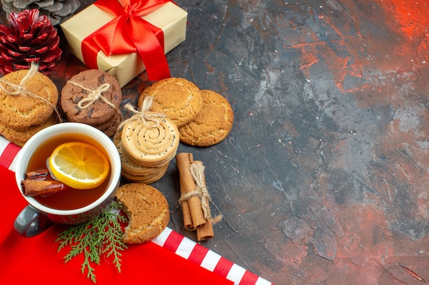 Vista superior de diferentes galletas atadas con una cuerda taza de té palitos de canela bloques de madera en el espacio libre de la mesa de color rojo oscuro