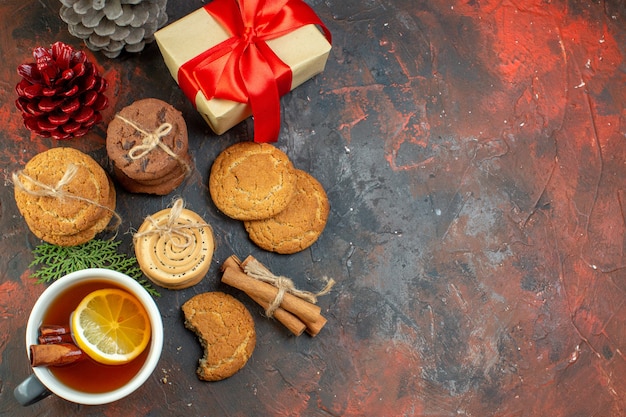 Vista superior de diferentes galletas atadas con una cuerda taza de té piñas regalo en la mesa de color rojo oscuro con lugar de copia