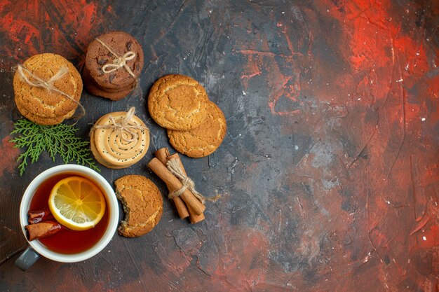 Vista superior de diferentes galletas atadas con una taza de té de cuerda en el espacio de copia de la mesa de color rojo oscuro