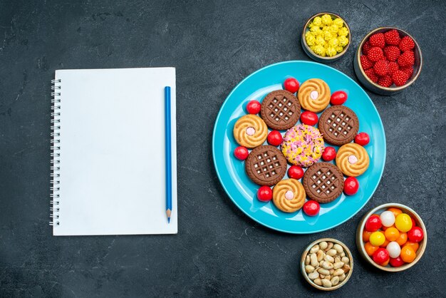 Vista superior de diferentes galletas de azúcar con caramelos dentro de la placa en la superficie gris caramelo dulce galleta galleta azúcar