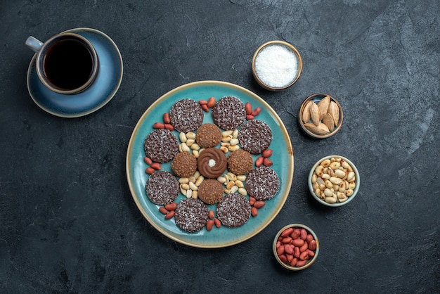 Vista superior de diferentes galletas a base de chocolate con nueces y una taza de café en la superficie gris caramelo bombón azúcar dulce pastel de galletas