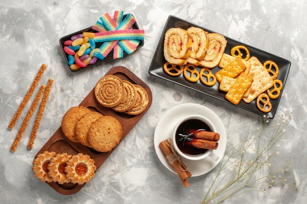 Vista superior de diferentes galletas con caramelos y una taza de té en la superficie blanca galletas bizcocho de azúcar hornear pastel pastel dulce