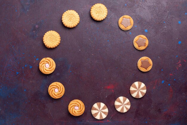 Vista superior de diferentes galletas con crema en el interior sobre una superficie oscura