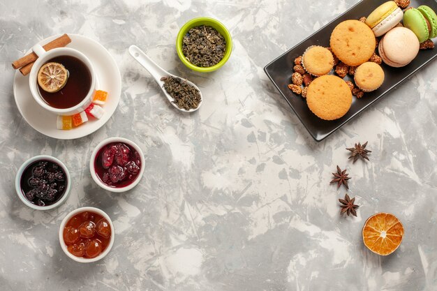 Vista superior de diferentes galletas con diferentes mermeladas y taza de té sobre fondo blanco galleta pastel de azúcar pastel galletas dulces