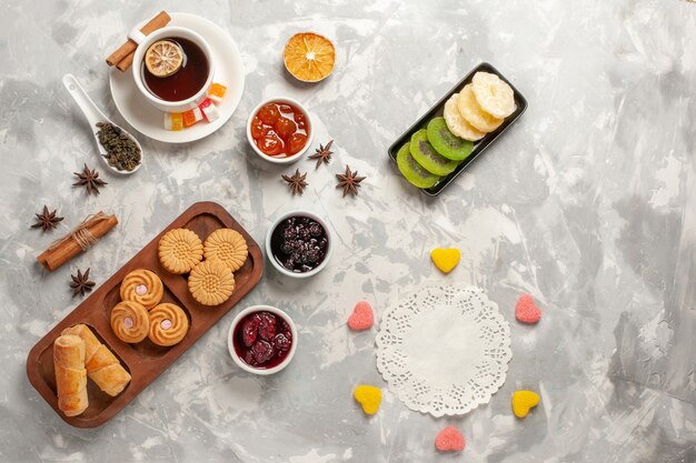 Vista superior de diferentes galletas con frutos secos y una taza de té en la superficie blanca clara galleta pastel de pastel de azúcar galleta dulce