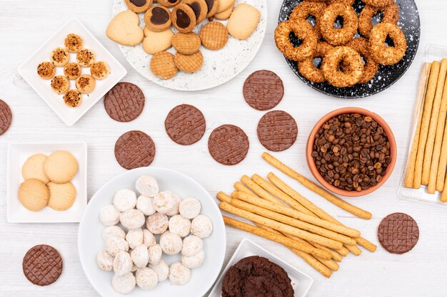 Vista superior diferentes galletas granos de café y palitos de pan en la mesa blanca