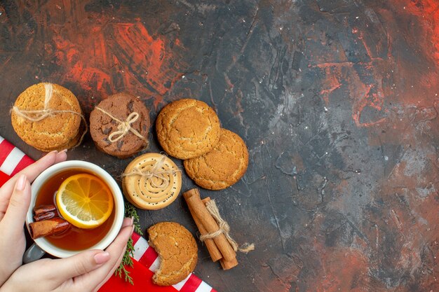 Vista superior de diferentes galletas taza de té palitos de canela en el espacio libre de la mesa de color rojo oscuro