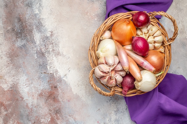 Vista superior de diferentes ingredientes cebollas y ajo dentro de la canasta con tejido morado