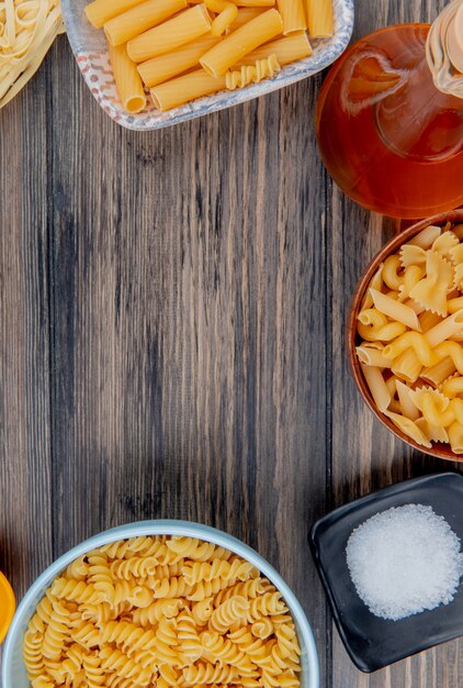 Vista superior de diferentes macarrones como ziti rotini tagliatelle y otros con sal de mantequilla derretida en madera con espacio de copia