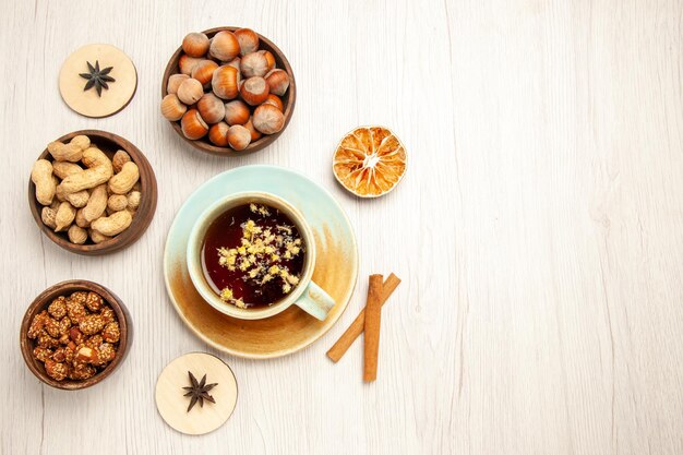 Vista superior de diferentes nueces dentro de pequeñas ollas con una taza de té en el escritorio blanco nueces bocadillo nuez avellana