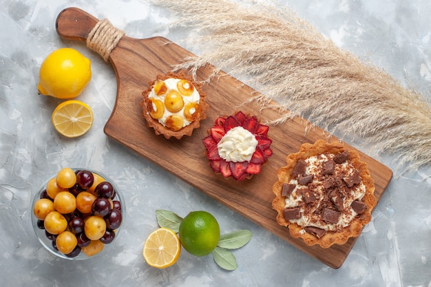 Vista superior de diferentes pasteles cremosos pasteles afrutados con limón y cerezas en el escritorio blanco pastel hornear galletas dulces azúcar fruta