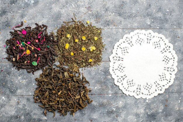 Vista superior de diferentes sabores secos de té fresco en el escritorio rústico gris