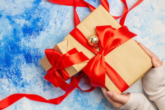 Vista superior de diferentes tamaños de regalos atados con cinta roja en la mano de la mujer en el cuadro blanco azul