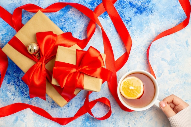 Foto gratuita vista superior de diferentes tamaños de regalos atados con cinta roja, una taza de té en la mano de la mujer en el cuadro blanco azul