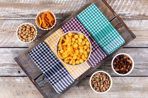 Vista superior de diferentes tipos de aperitivos como nueces, galletas y galletas en servilletas en la superficie de madera blanca horizontal