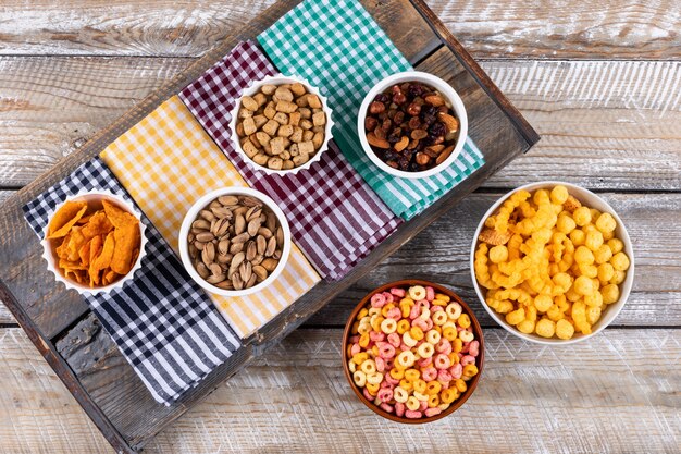 Vista superior de diferentes tipos de aperitivos como nueces, galletas y galletas en servilletas en la superficie de madera blanca horizontal