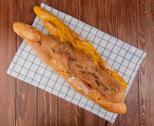 Vista superior de diferentes tipos de baguette sobre tela escocesa y fondo de madera