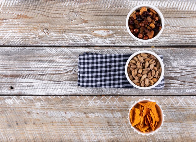 Vista superior de diferentes tipos de bocadillos como chips de nueces en servilleta con espacio de copia sobre fondo blanco de madera horizontal