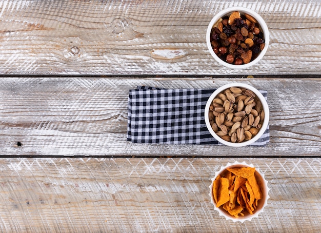 Vista superior de diferentes tipos de bocadillos como chips de nueces en servilleta con espacio de copia sobre fondo blanco de madera horizontal