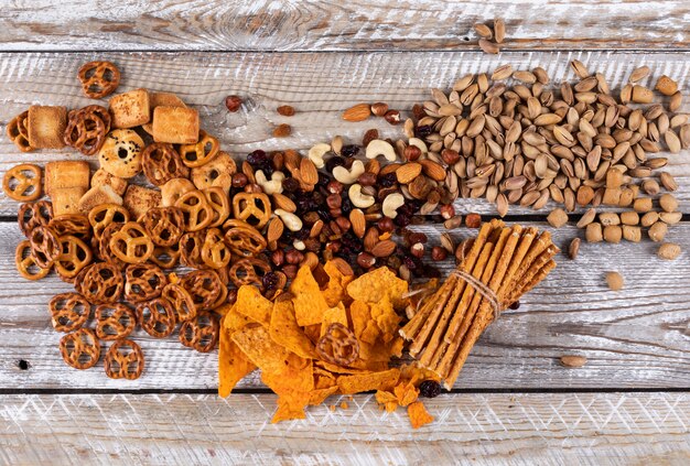 Vista superior de diferentes tipos de bocadillos como nueces, galletas y galletas en la superficie de madera blanca horizontal