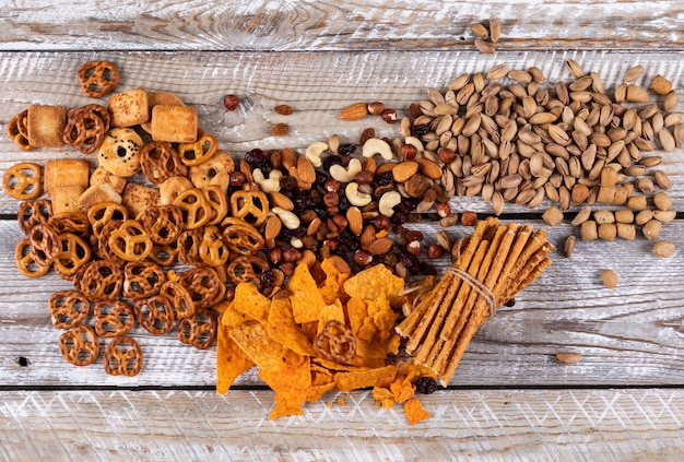 Vista superior de diferentes tipos de bocadillos como nueces, galletas y galletas en la superficie de madera blanca horizontal