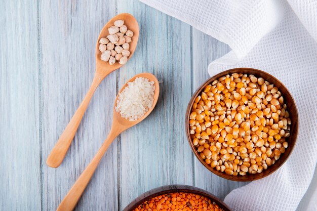 Vista superior de diferentes tipos de granos y semillas en cuencos y cucharas de madera lentejas rojas semillas de maíz arroz y garbanzos