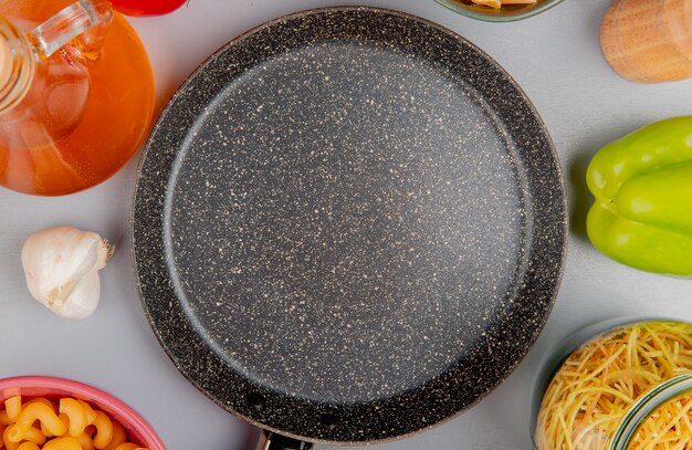 Foto gratuita vista superior de diferentes tipos de pasta como cavatappi y otros con ajo, tomate, mantequilla, pimiento alrededor de la sartén sobre la superficie púrpura