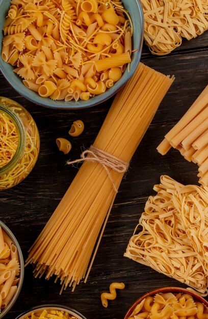 Vista superior de diferentes tipos de pasta como espaguetis fideos tagliatelle y otros sobre superficie de madera