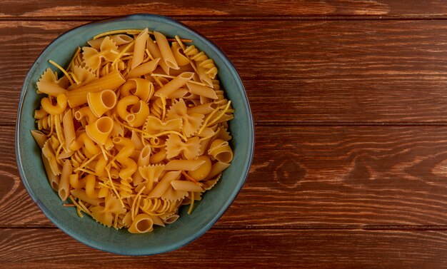 Vista superior de diferentes tipos de pasta en un tazón sobre superficie de madera con espacio de copia