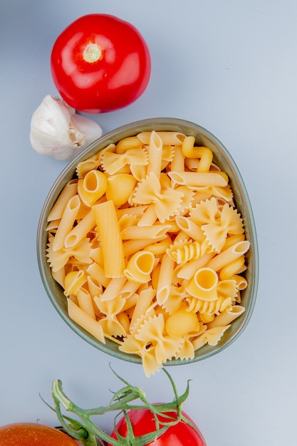 Vista superior de diferentes tipos de pasta en un tazón con tomate ajo sobre superficie azul