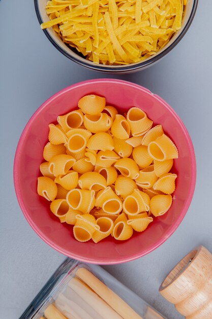 Vista superior de diferentes tipos de pasta en tazones como tagliatelle bucatini pipe-rigate sobre superficie azul