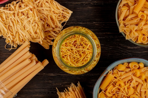 Vista superior de diferentes tipos de pastas como tallarines de espagueti bucatini y otros tallarines sobre superficie de madera