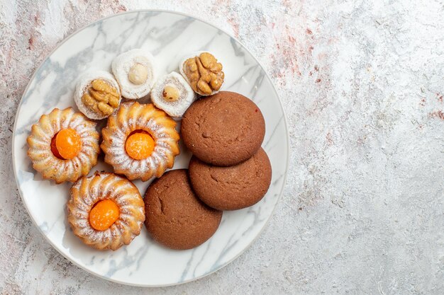 Vista superior de diferentes tortas dulces pequeños sobre fondo blanco claro galleta galleta azúcar té dulce pastel