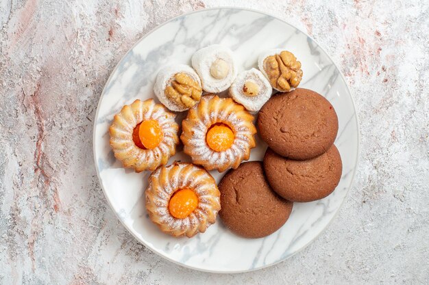 Vista superior de diferentes tortas dulces pequeños sobre fondo blanco galletas galleta azúcar té dulce pastel