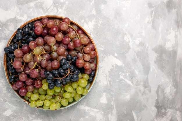 Vista superior de diferentes uvas jugosas frutas amargas suaves en el escritorio blanco claro