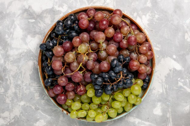 Vista superior de diferentes uvas jugosas frutas amargas suaves en el escritorio blanco claro