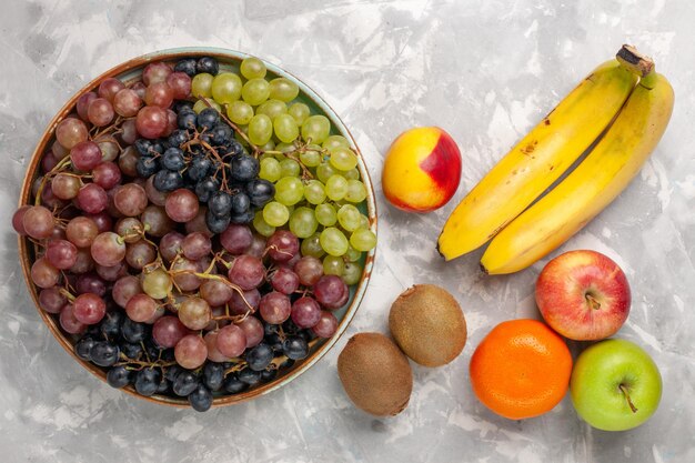 Vista superior de diferentes uvas con otras frutas en el escritorio blanco claro