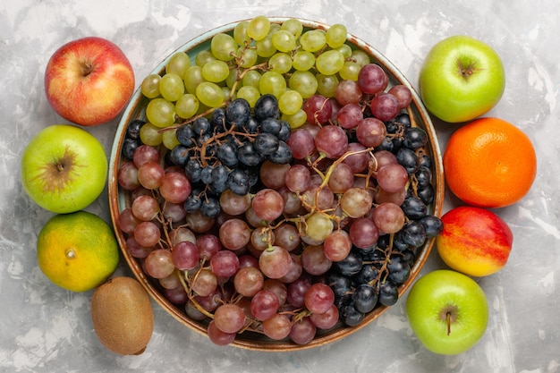 Vista superior de diferentes uvas con otras frutas frescas en el escritorio blanco claro