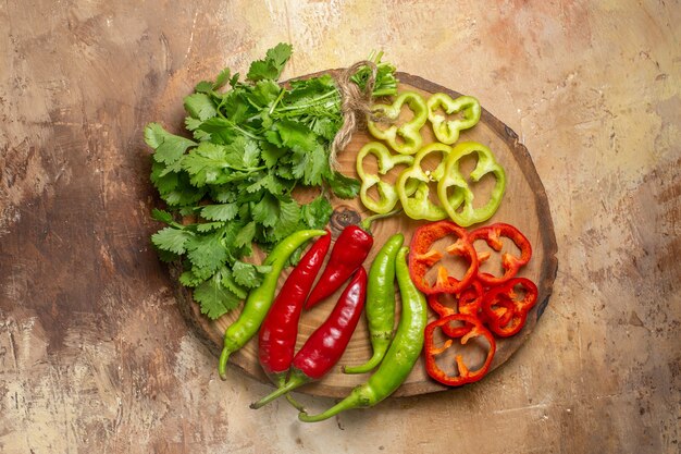 Vista superior de diferentes verduras cilantro pimientos picantes pimientos cortados en trozos en un tablero de madera de árbol redondo sobre fondo ámbar