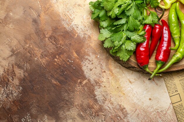 Vista superior de diferentes verduras cilantro pimientos picantes en un tablero de madera de árbol redondo un periódico sobre fondo ámbar