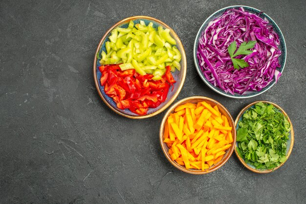 Vista superior de diferentes verduras en rodajas con verduras en la dieta de salud de ensalada de mesa oscura