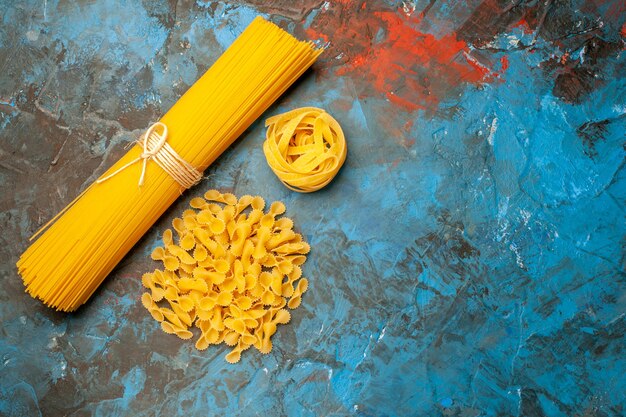 Vista superior de diversas pastas italianas para la preparación de la cena en el lado derecho sobre fondo azul.