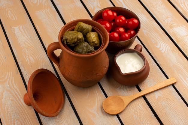 Vista superior de dolma en maceta junto con tomates rojos y yogurt en el piso de madera