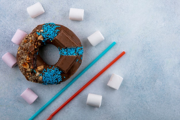 Foto gratuita vista superior de donut de chocolate con malvaviscos y azul con pajitas rojas sobre una superficie gris