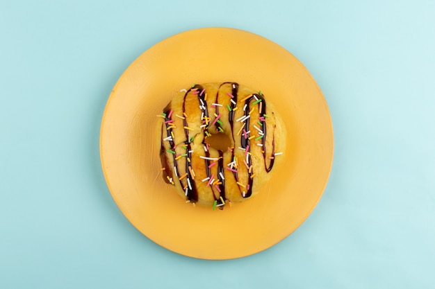 Foto gratuita vista superior donut con líneas de choco y caramelos de colores dentro de la placa naranja en el piso azul hielo