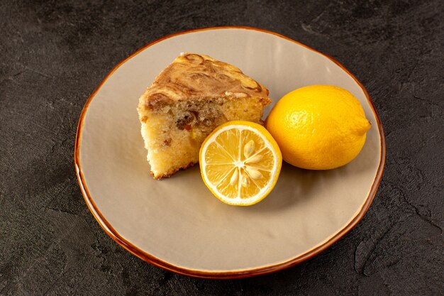 Una vista superior dulce pastel delicioso delicioso pastel de choco rebanada dentro de un plato beige junto con limones amarillos en el fondo oscuro galletas de té de azúcar hornear