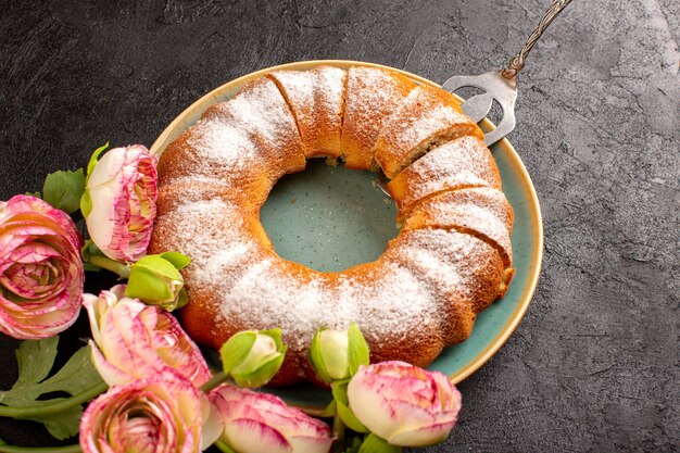 Una vista superior dulce pastel redondo con azúcar en polvo en la parte superior en rodajas dulce delicioso aislado dentro de la placa junto con flores y fondo gris galleta galleta de azúcar