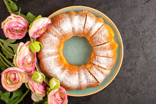 Una vista superior dulce pastel redondo con azúcar en polvo en la parte superior en rodajas dulce delicioso aislado dentro de la placa junto con flores y fondo gris galleta galleta de azúcar