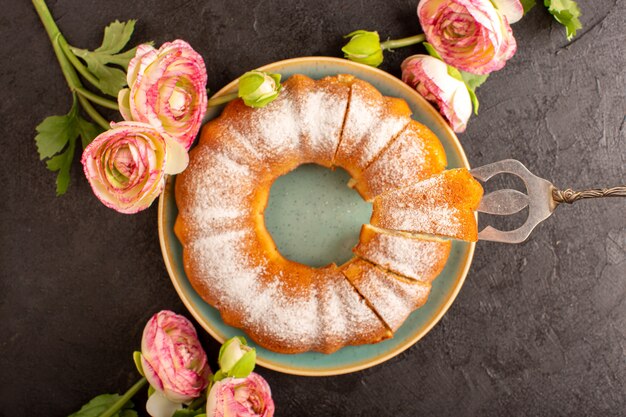 Una vista superior dulce pastel redondo con azúcar en polvo en la parte superior en rodajas dulce delicioso aislado dentro de la placa junto con flores y fondo gris galleta galleta de azúcar