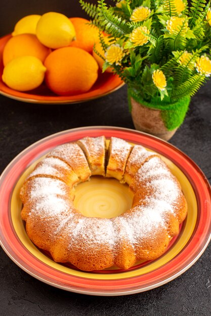 Foto gratuita una vista superior dulce pastel redondo con azúcar en polvo en rodajas dulce delicioso pastel aislado dentro de la placa junto con limones y galleta de azúcar de fondo gris